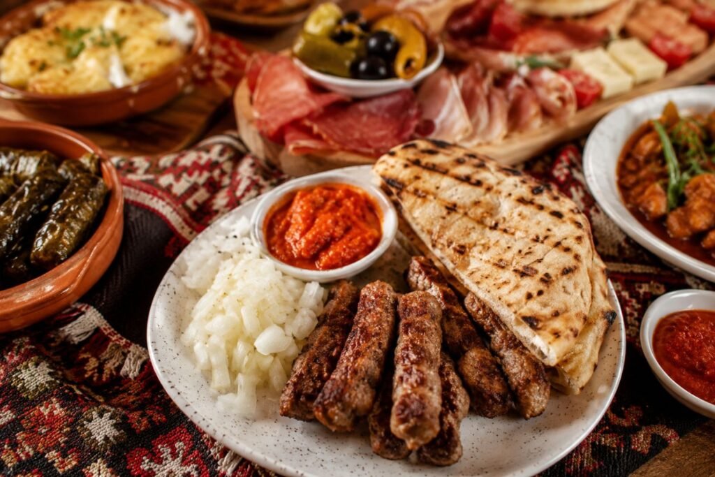 Croatian food spread on a wooden table, including grilled meats, flatbread, olives, cured meats, stuffed grape leaves, ajvar, and traditional Balkan dishes arranged in a warm, inviting setting.