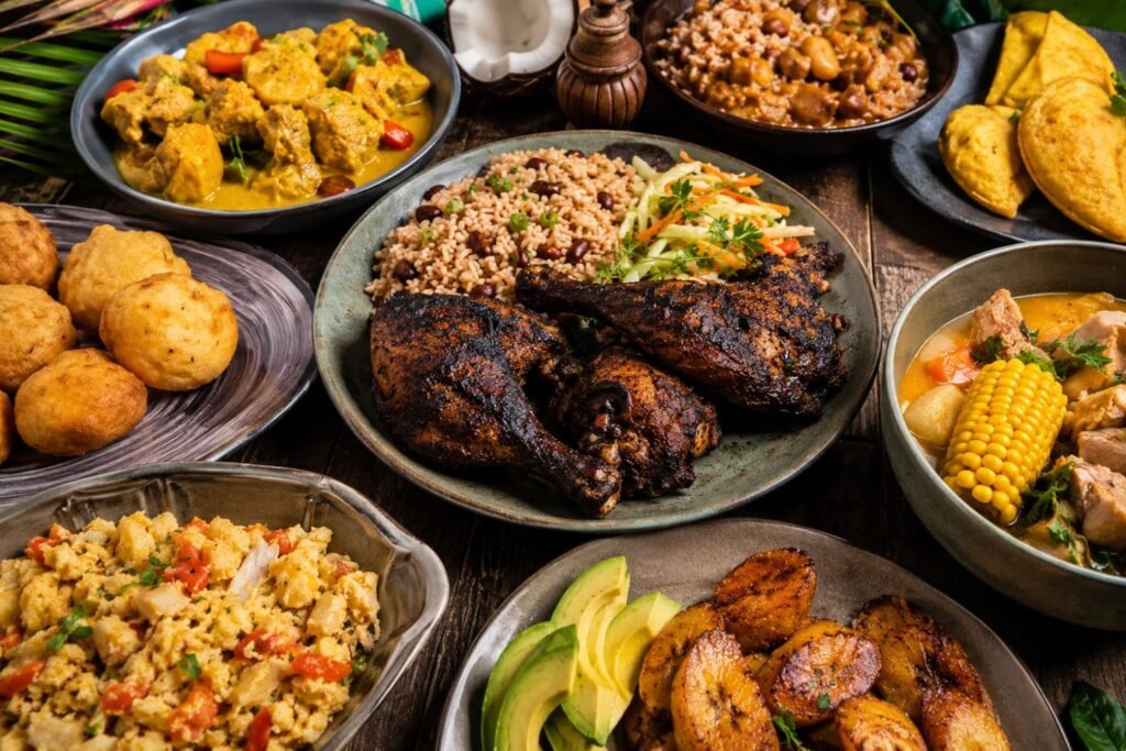 An overhead view of a vibrant Jamaican food feast featuring jerk chicken, rice and peas, curry dishes, fried plantains, soup, festival bread, avocado slices, and traditional island side dishes arranged on rustic serving plates and bowls.